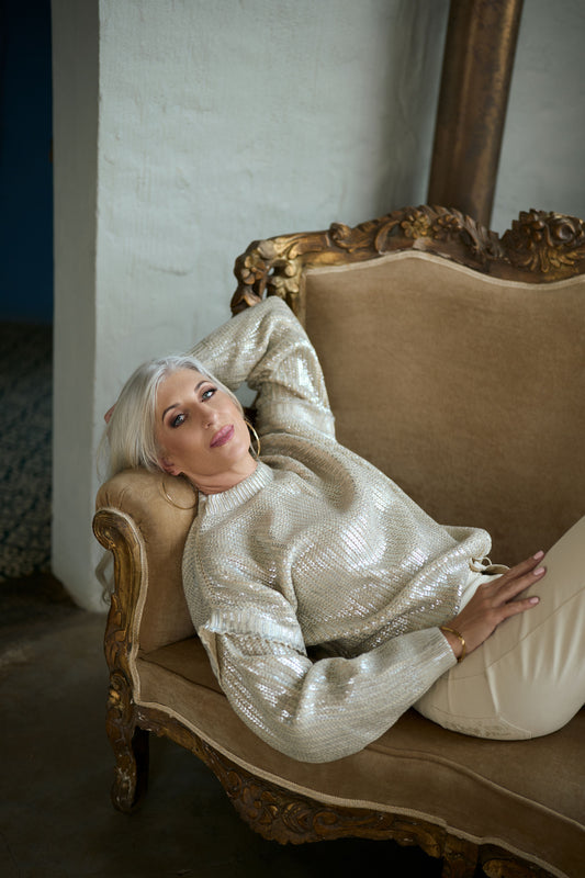 Woman in a sparkly silver outfit sitting on an ornate chair.