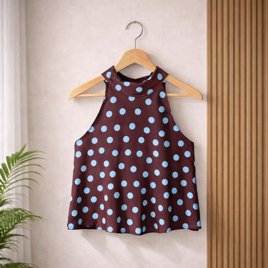 Elegant sleeveless high neck top featuring a classic polka dot print, flowy silhouette, and lightweight fabric in black, blush, and chocolate colourways, styled on a wooden hanger.