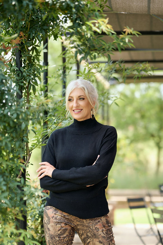 Women’s black poloneck sweater with long sleeves and fitted knit design styled with patterned pants – classic winter turtleneck fashion.