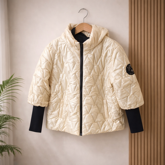 light gold quilted jacket with black sleeves on a hanger against a neutral wall.
