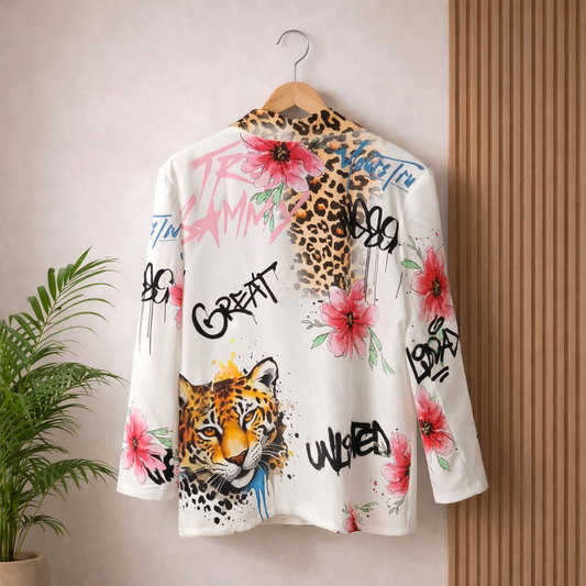 White artistic blazer with pink floral prints, leopard face, and graffiti text hanging on wooden hanger against light wall — fashion photography showcasing bold street‑art design.