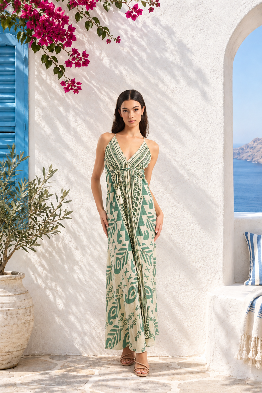 Woman wearing a cream maxi dress with green geometric patterns, a V-neckline, adjustable spaghetti straps, a cinched waist with tie detail, and a flowing ankle-length skirt.