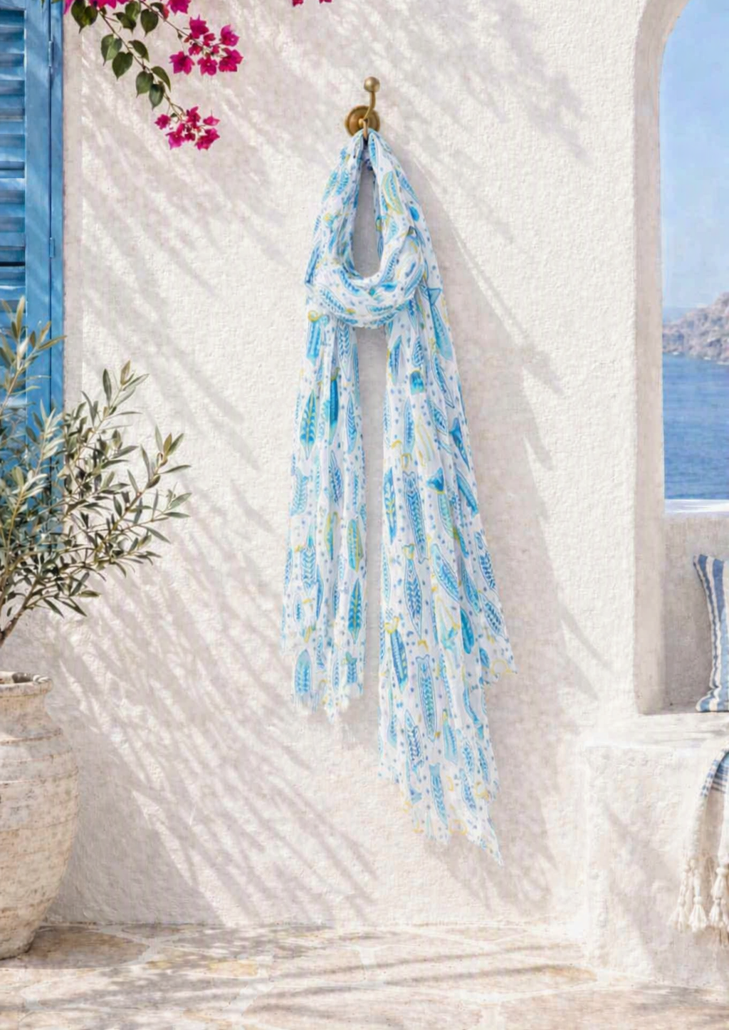 White lightweight scarf with repeating blue fish pattern in varying shades — semi‑transparent fabric, rolled and draped for casual wea