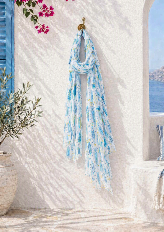 White lightweight scarf with repeating blue fish pattern in varying shades — semi‑transparent fabric, rolled and draped for casual wea
