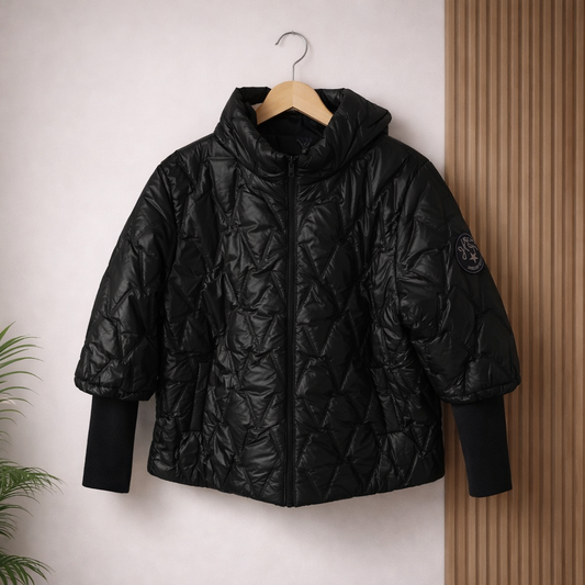 Black quilted jacket on a wooden hanger against a light wall with a wooden panel.