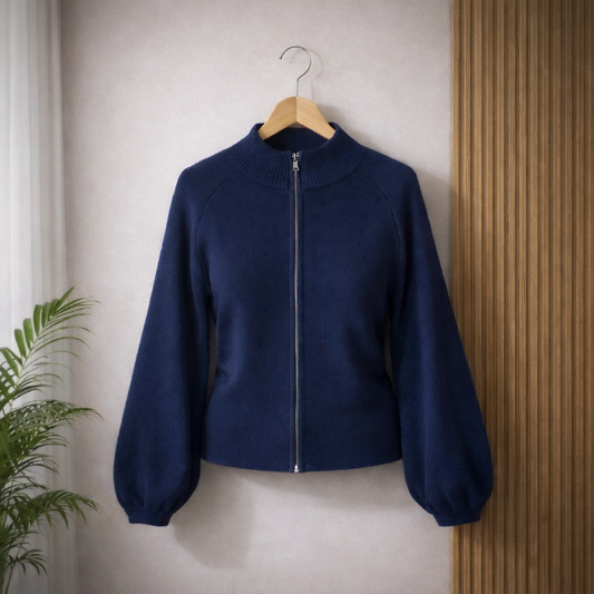 A navy blue zip-up sweater with ribbed collar, cuffs, and hem hanging on a wooden hanger against a light wal