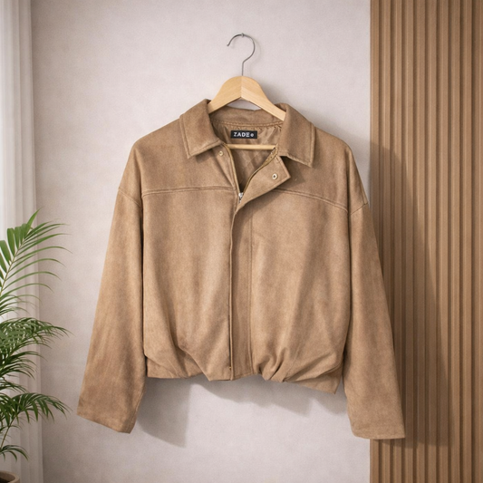Brown suede jacket on a hanger against a neutral wall with a plant to the left.