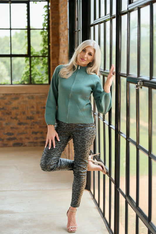 Model wearing ZADE Collection charcoal grey and black leopard print skinny pants with a green zip-up knit sweater and heels.