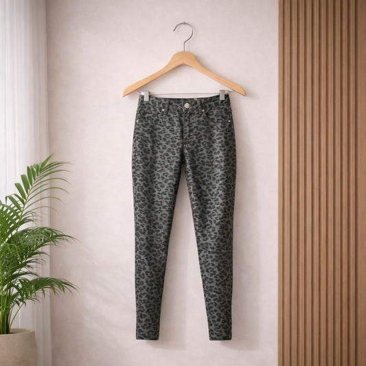 Leopard print pants on a wooden hanger against a neutral wall with a plant in the corner.