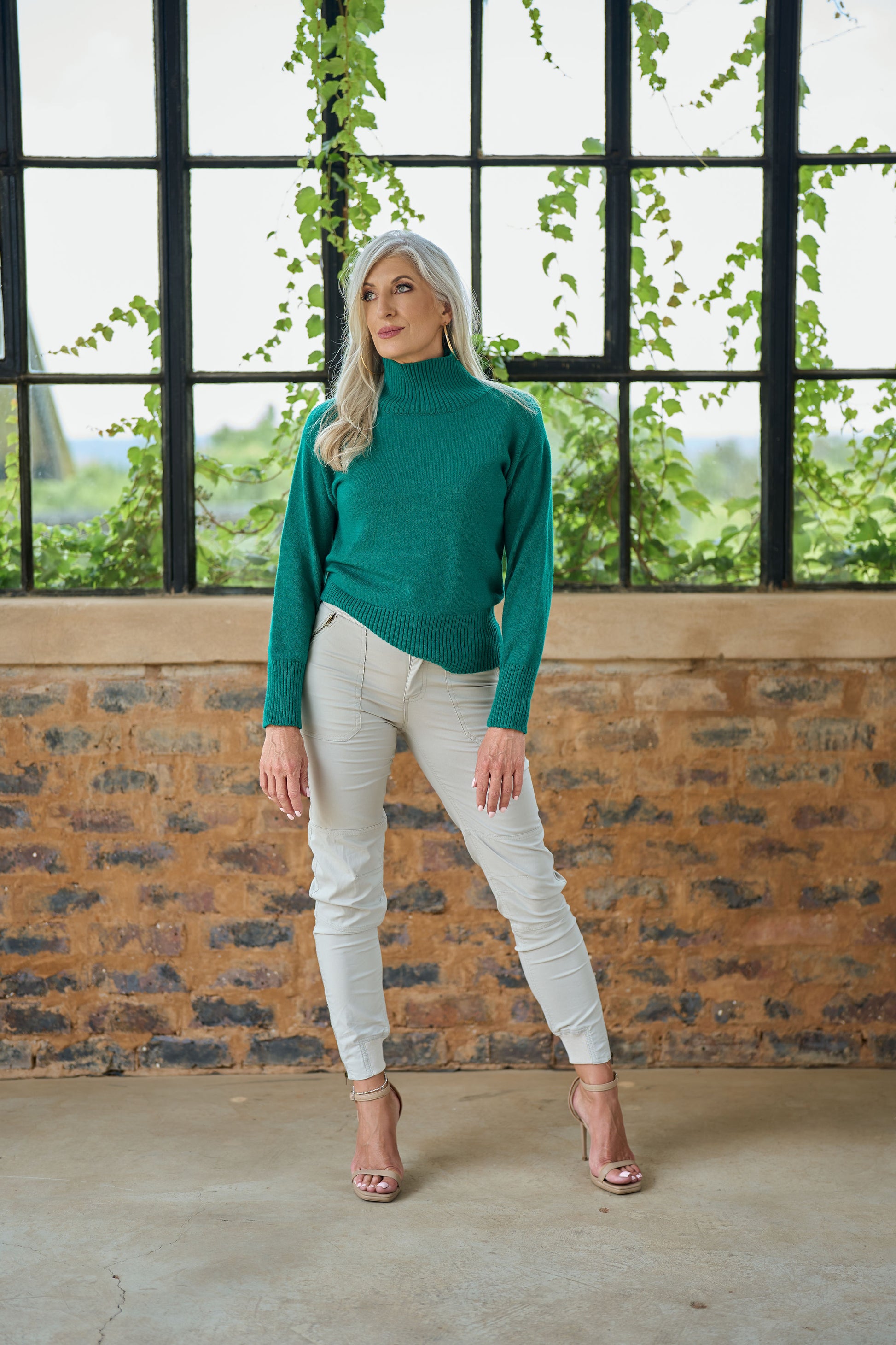 Model wearing ZADE Collection slim-fit cream cargo pants with zipper details and tapered ankles in an industrial outdoor setting.